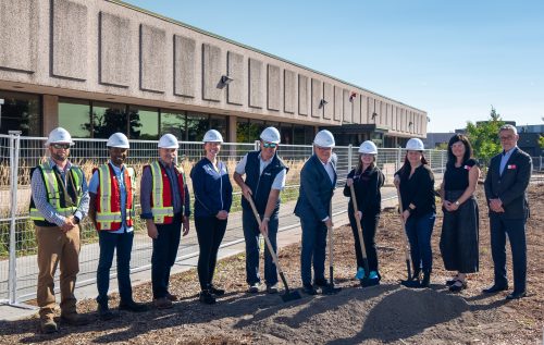 A group of people in white hard hats, some with shovels in the ground to signify the breaking ground on a new front entrance and athletic facilities at the Belleville campus.