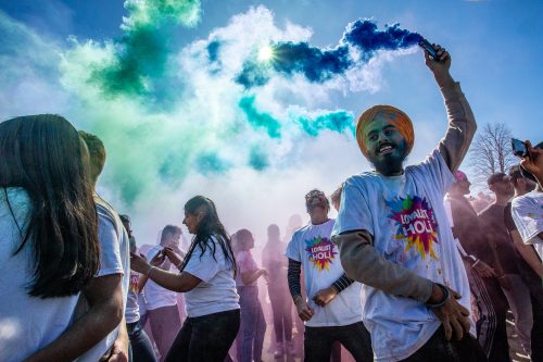 Students in a crowd dancing. One student has a colour flare putting up a cloud of blue and green smoke.