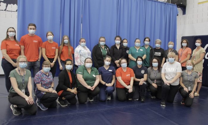 A group photo of students from various programs in the Loyalist College gym, wearing masks. Some kneeling in the front row, some standing in the back row.