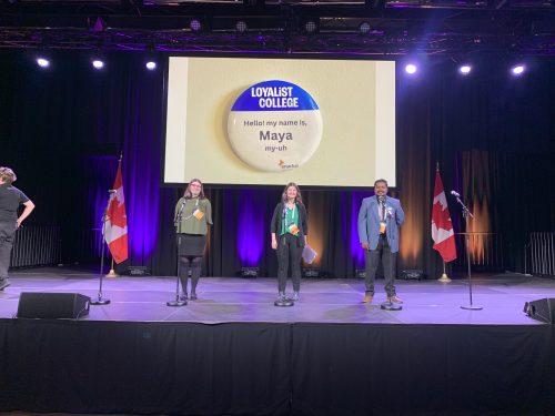 Loyalist students and Enactus members Maya Phaneuf, Arvind Sharma and Madison Bernard standing on stage at the Enactus National Challenge.