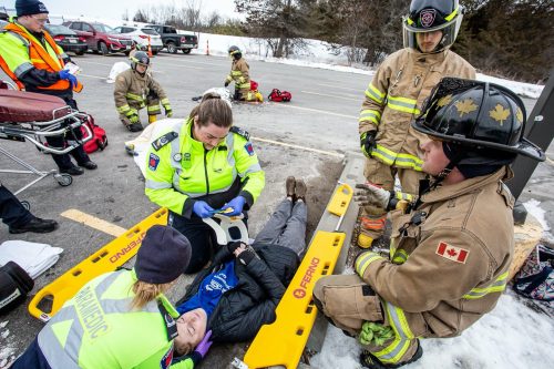 Two Paramedic students and two Pre-Service Firefighter students are gathered around a person laying on the ground, simulating treating the person in a mock accident.