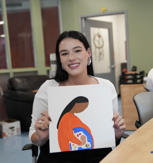 A woman posing, holding a painting of a woman wearing orange.