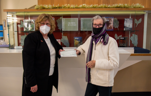 Dr. Ann Marie Vaughan, Loyalist President and CEO, with Eurithe Purdy. Purdy is holding a cheque and they're both standing in front of a display case and wearing masks.