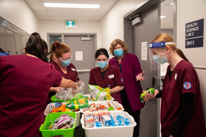 Dr. Ann Marie Vaughan, President and CEO, with Personal Support Worker students wearing maroon scrubs around a snack cart. Everyone is wearing masks.