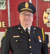 A headshot of Deputy Fire Chief, Rick Caddick wearing his uniform in front of a fire truck.