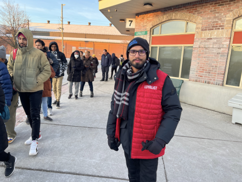 A Loyalist student in a red Loyalist vest at the Belleville bus terminal. In the background is a lineup of people.