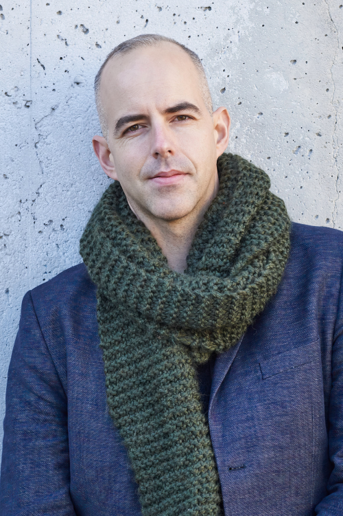 A headshot of Janak Alford, in front of a concrete background.