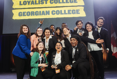 A large group of Loyalist students and Loyalist Enactus members posing on a stage.