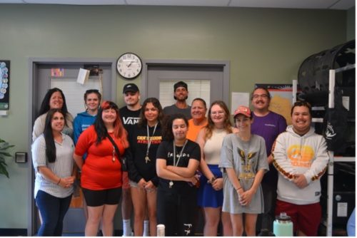 A mixed group of students and staff standing indoors, posed and smiling.