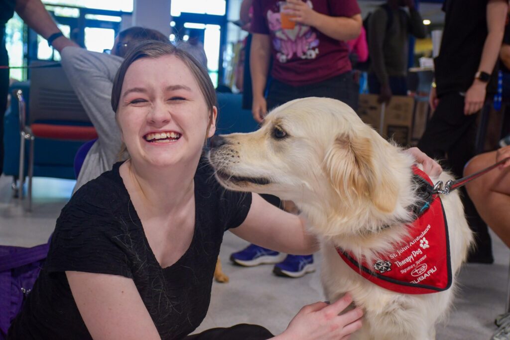 Student smiling with a therapy dog during a campus visit.