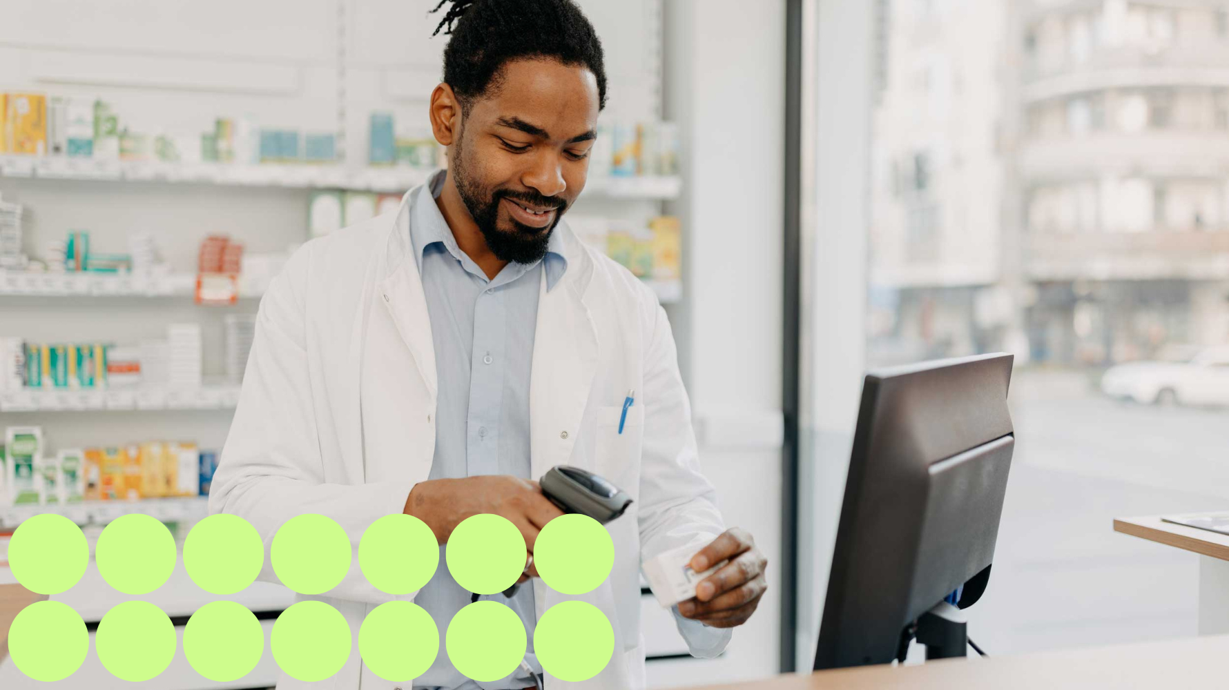 A pharmacy technician in a white lab coat scans a medication package at the counter of a modern pharmacy. Shelves stocked with pharmaceutical products are visible in the background, and a computer monitor is on the counter. A green circle graphic is included on the bottom left.