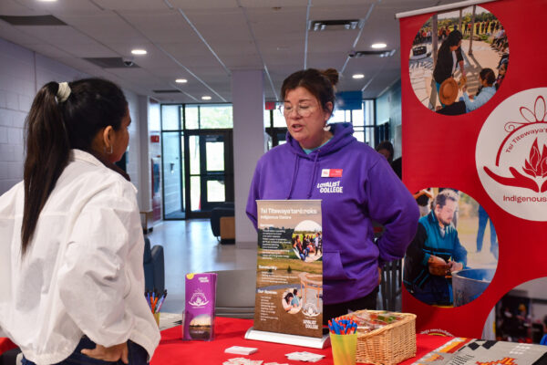 A staff member in a purple hoodie speaking to a student at a service fair.