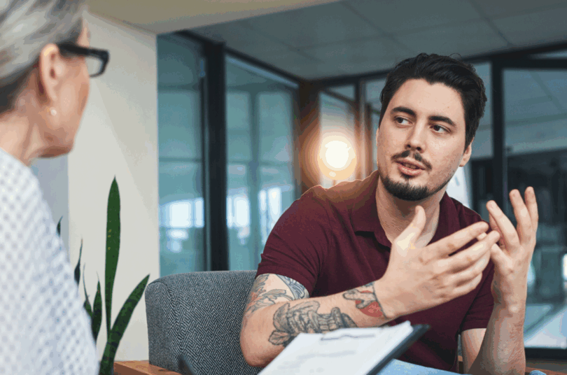 Young man with tattoos in conversation with a counsellor in an office setting.