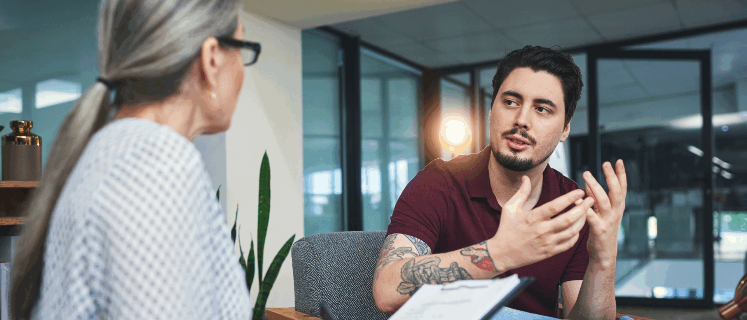 Young man with tattoos in conversation with a counsellor in an office setting.