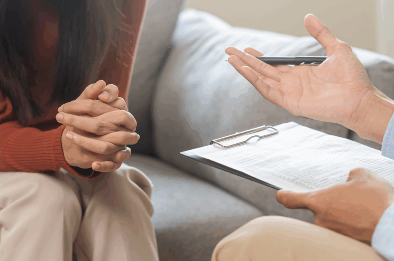 Person holding a clipboard talking with a woman during a counselling session.