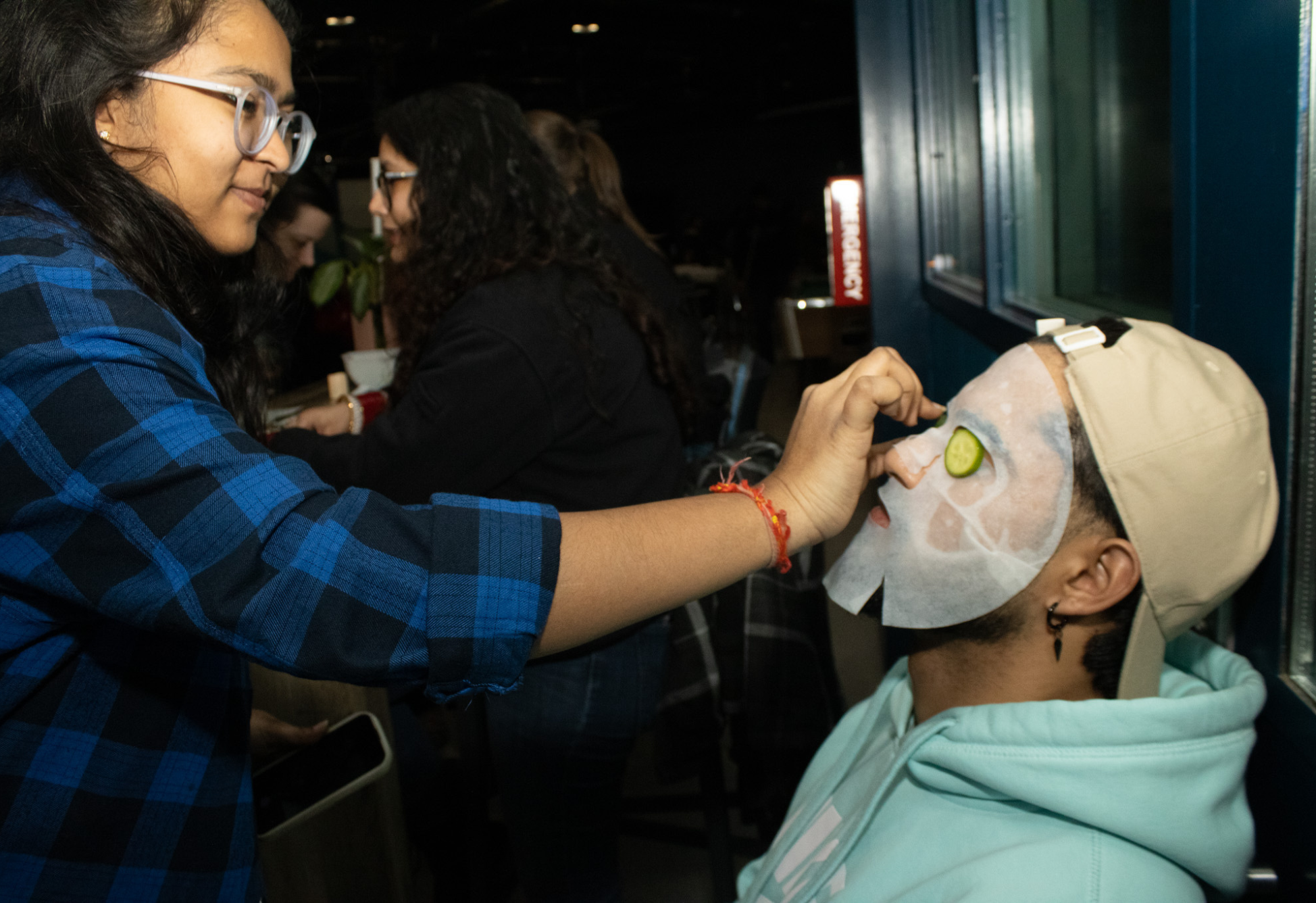 A student gently places cucumber slices over another student’s face mask during a self-care event.