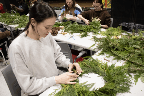 Students sit at tables crafting holiday wreaths from fresh greenery and pinecones.