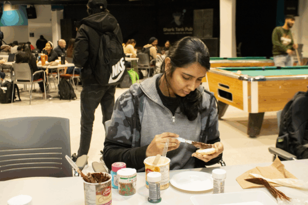 A student decorates a cookie with chocolate icing at a table filled with baking supplies.