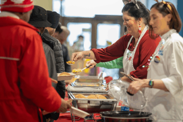 Staff wearing holiday attire serve food to students from buffet trays during a festive meal event.