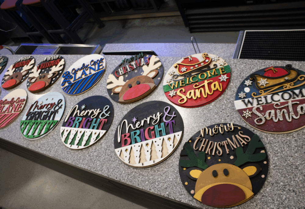 Colourful handmade Christmas signs with festive designs are displayed across a countertop.