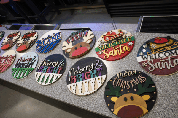 Colourful handmade Christmas signs with festive designs are displayed across a countertop.
