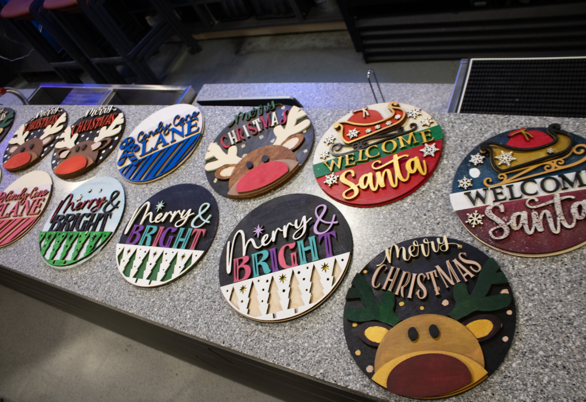 Colourful handmade Christmas signs with festive designs are displayed across a countertop.