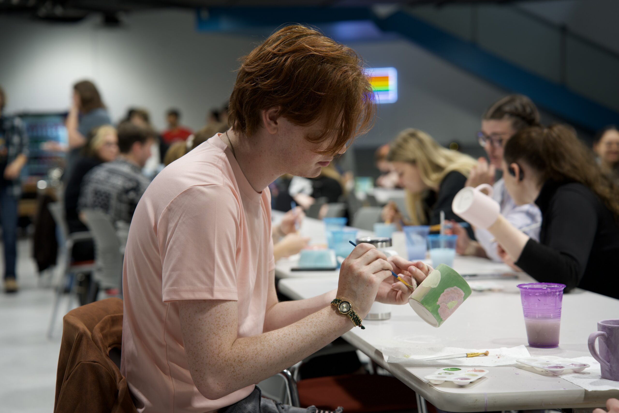 Individual seated at a table painting a ceramic mug during a group art activity.