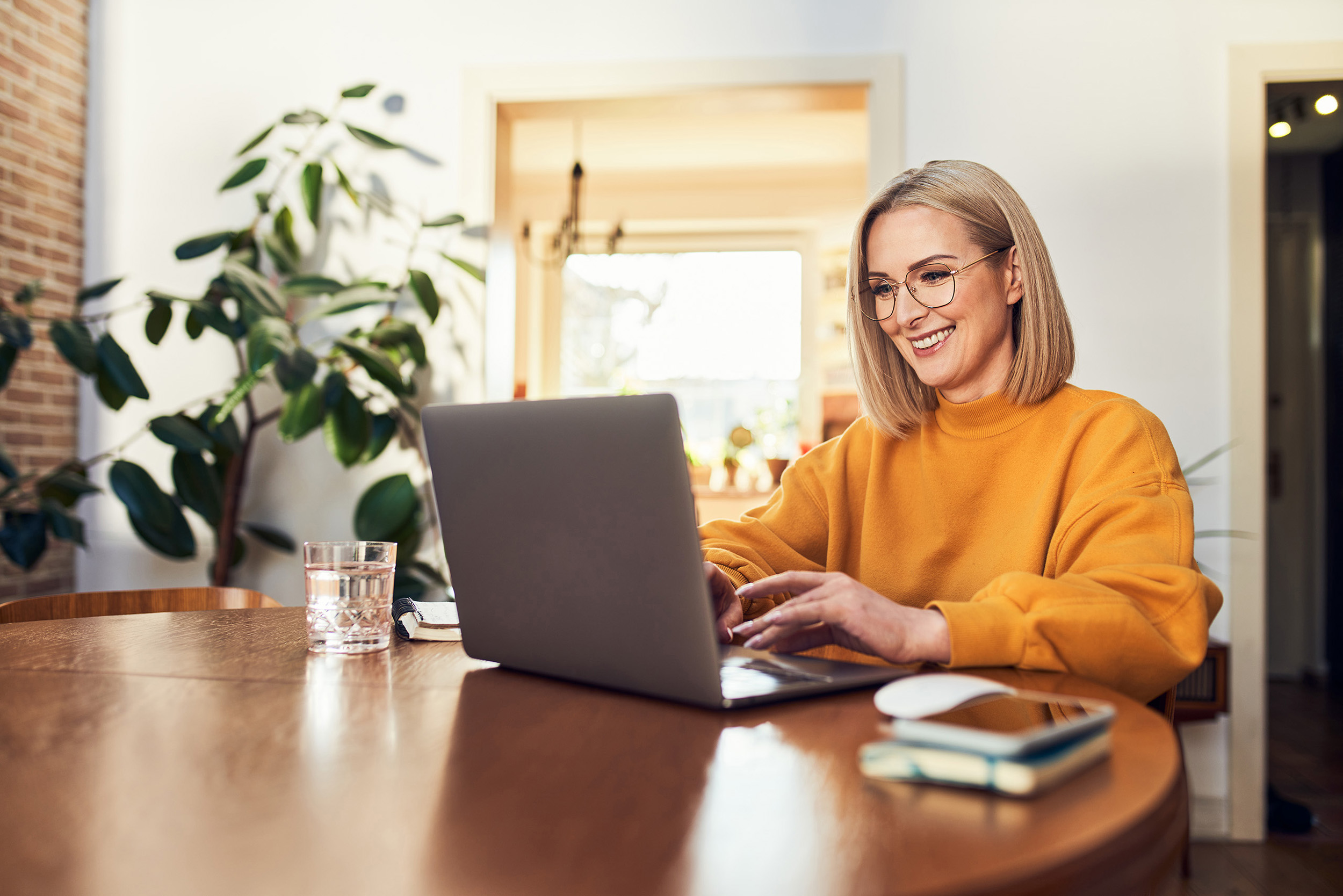 Happy mature woman using laptop while studying remotely from home in living room