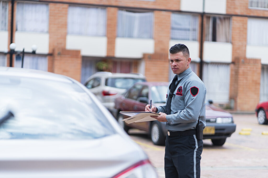 Security guard standing beside a parked car looking at a clipboard.