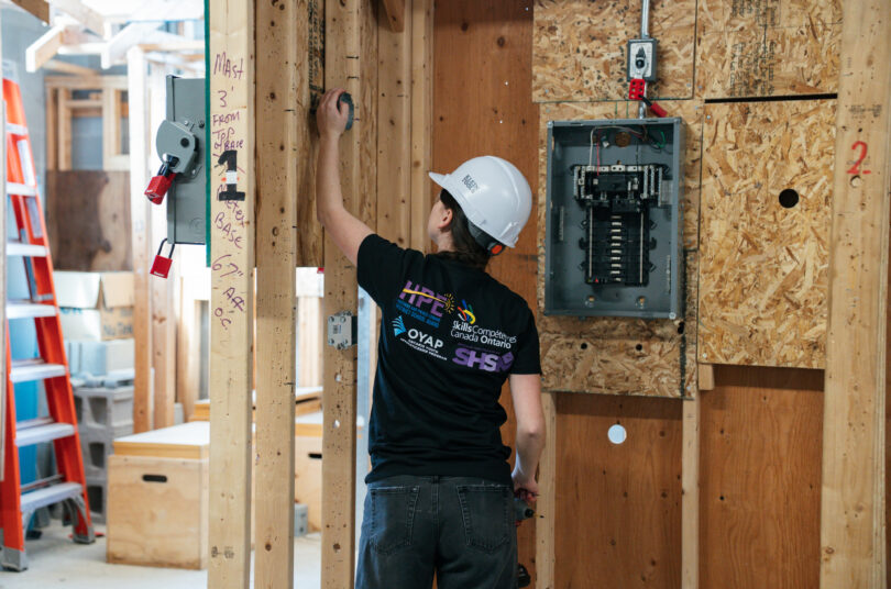Young woman working with an electrical panel in a white hard hat.