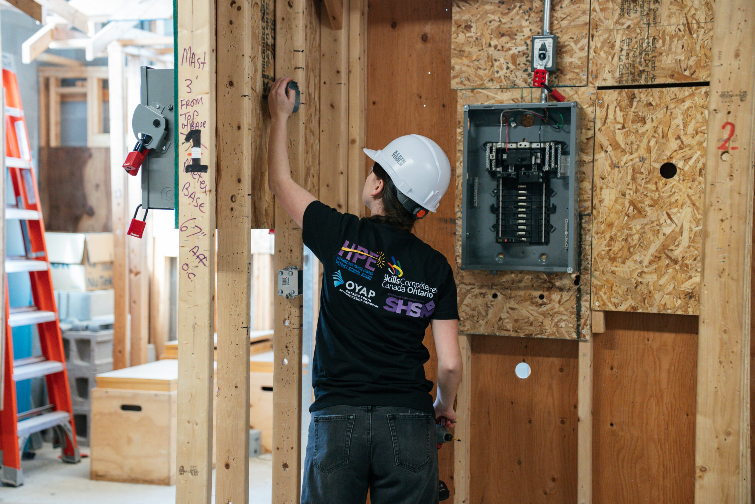 Young woman working with an electrical panel in a white hard hat.