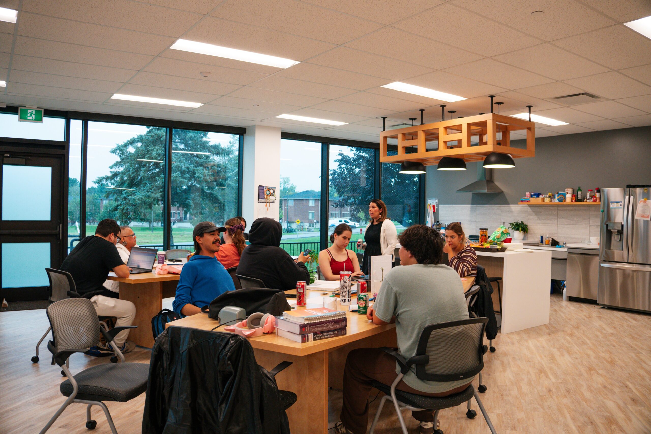 Students gathered around tables in the Indigenous Centre, with a shared kitchen in the background.